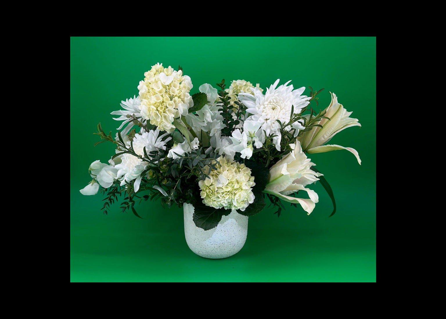 A lush floral arrangement in green and white, arranged in a white ceramic vase and placed against a green background.