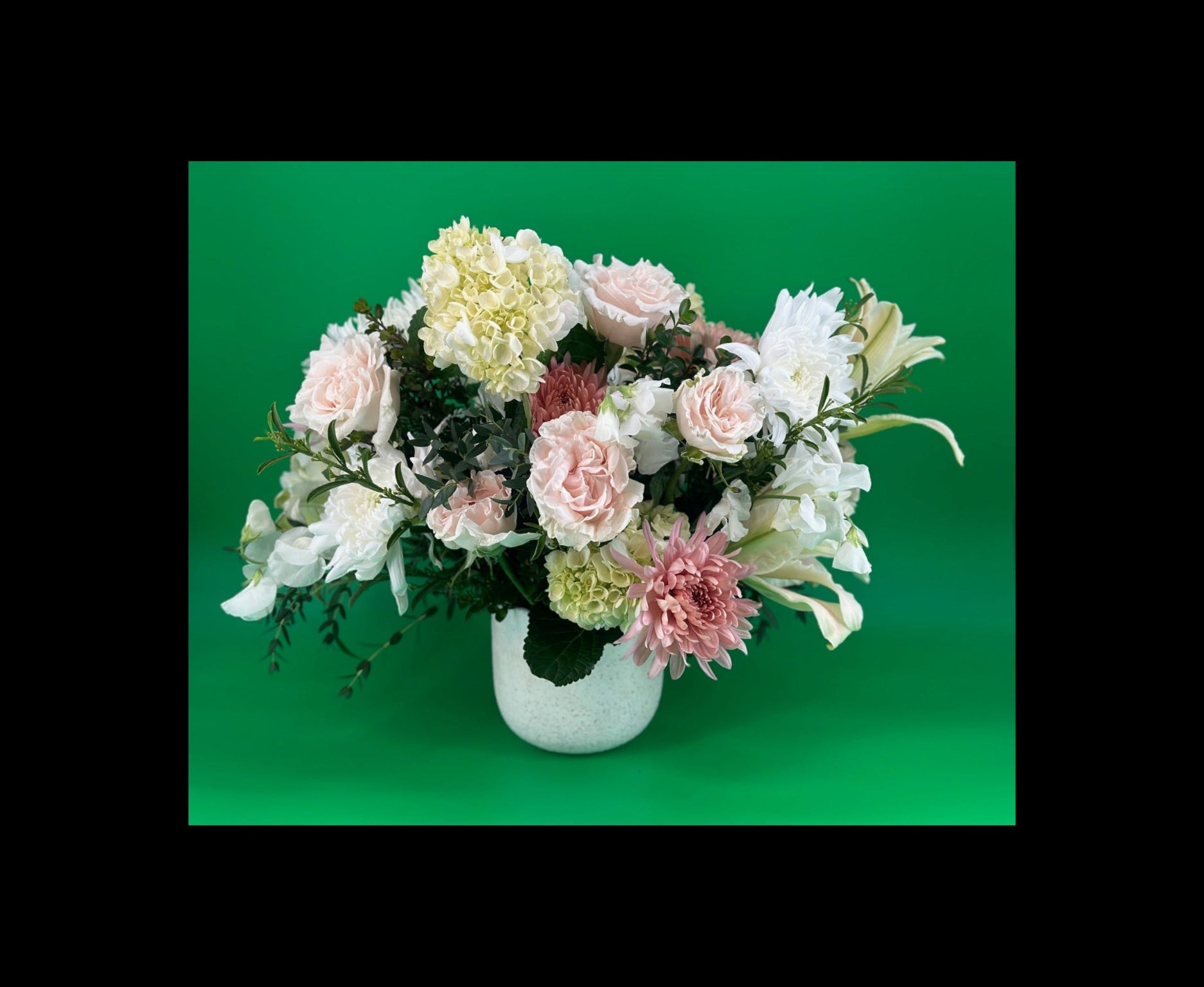 A lush floral arrangement in neutral colors inside a white ceramic container against a green background